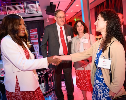 Photo of two women shaking hands while another woman and a man look on.